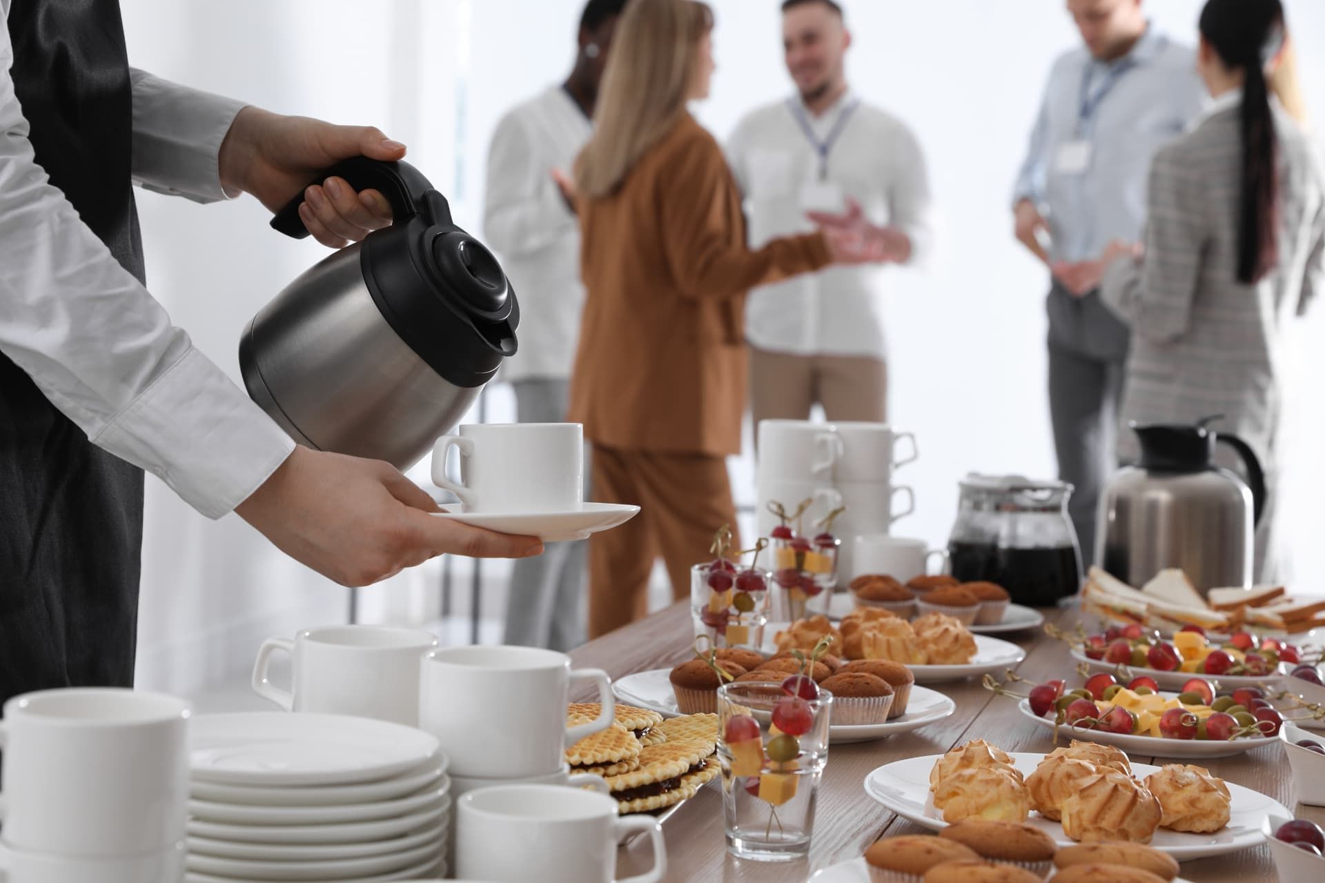 Caterer pouring coffee at an office breakfast spread with pastries and fruit